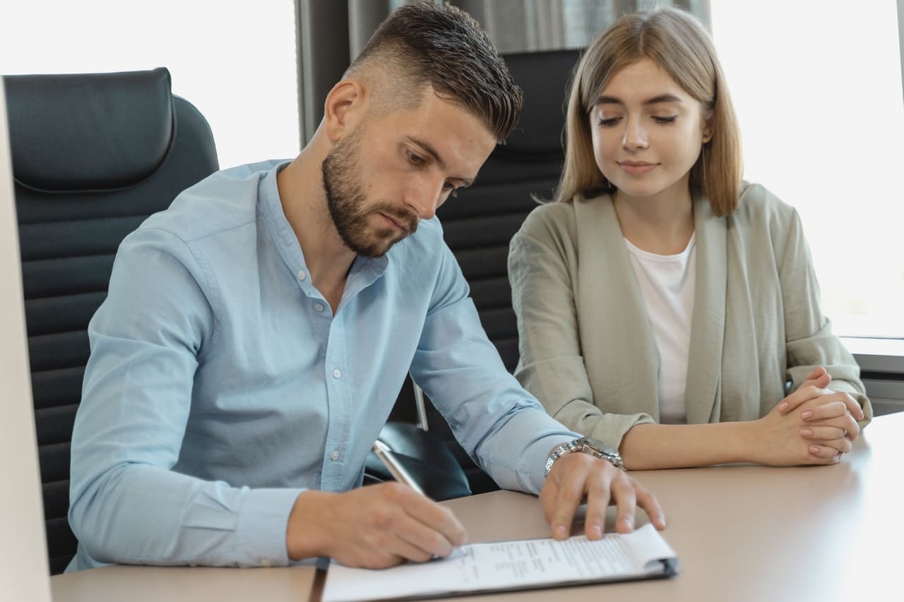 homme qui signe un contrat en étant assis à côté d'une femme